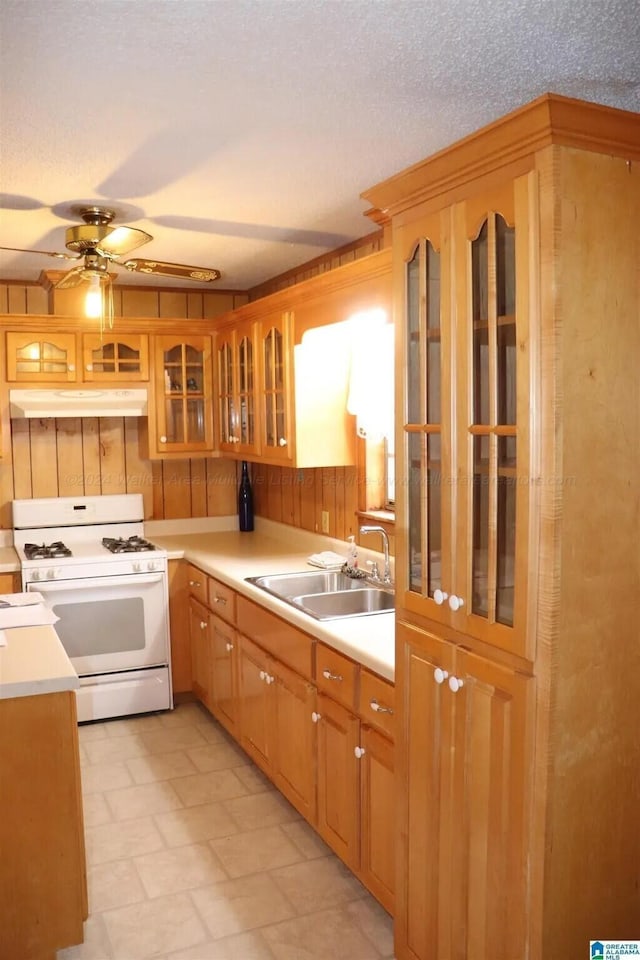 kitchen featuring white gas range, ceiling fan, sink, wood walls, and a textured ceiling