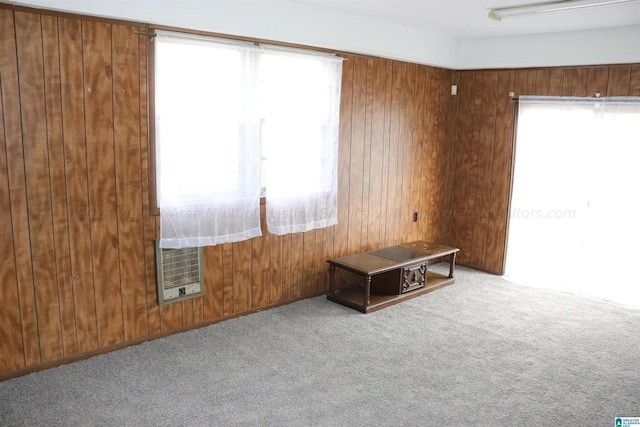 carpeted empty room with a healthy amount of sunlight, wooden walls, and heating unit