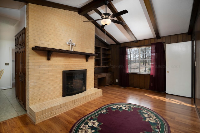 living room with wooden walls, a fireplace, lofted ceiling with beams, and light wood-type flooring