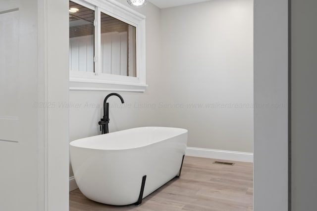 bathroom with a freestanding bath, wood finished floors, visible vents, and baseboards