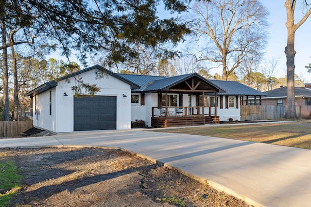 view of front of house with a garage, driveway, metal roof, covered porch, and fence