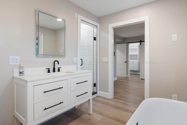 full bathroom featuring wood finished floors, vanity, baseboards, a freestanding bath, and a shower stall