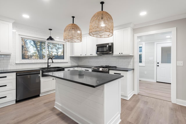 kitchen with appliances with stainless steel finishes, dark countertops, a sink, and light wood finished floors