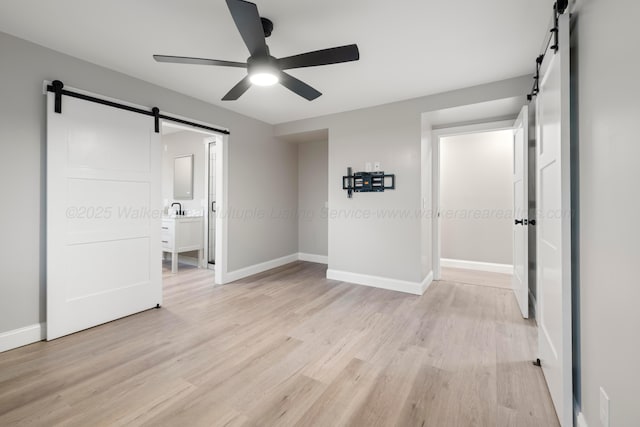 unfurnished bedroom with a barn door, baseboards, light wood-style flooring, and a sink