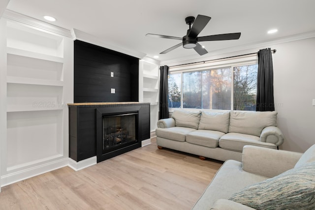 living area with built in features, a fireplace, light wood finished floors, a ceiling fan, and ornamental molding