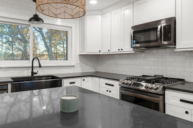 kitchen featuring pendant lighting, tasteful backsplash, appliances with stainless steel finishes, white cabinets, and a sink