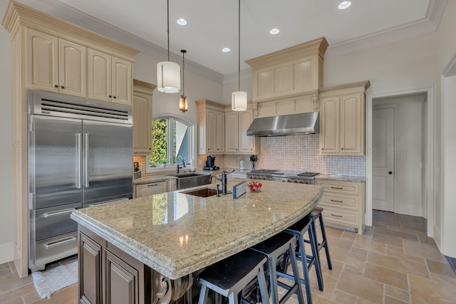 kitchen with cream cabinets, under cabinet range hood, appliances with stainless steel finishes, decorative backsplash, and crown molding