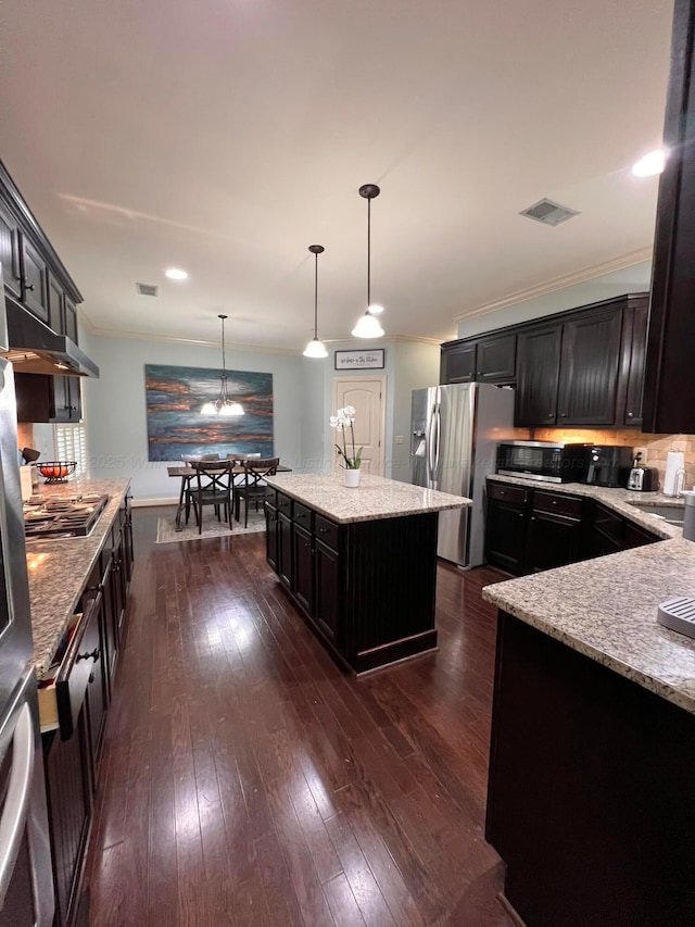 kitchen featuring hanging light fixtures, light stone countertops, appliances with stainless steel finishes, and a kitchen island