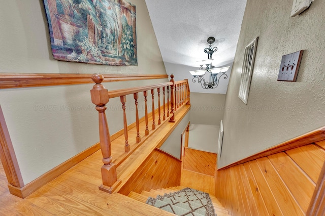 stairway featuring wood-type flooring, a textured ceiling, and a notable chandelier