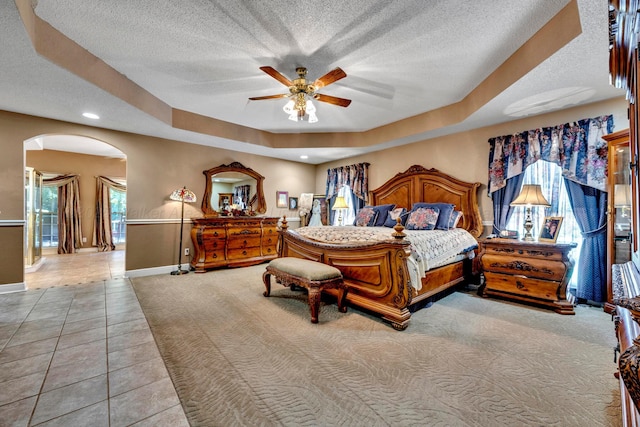 tiled bedroom featuring ceiling fan, a tray ceiling, and a textured ceiling