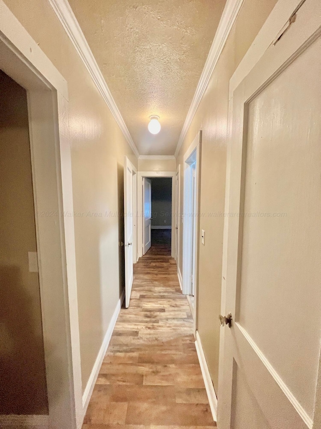 hallway with ornamental molding, a textured ceiling, and light hardwood / wood-style flooring