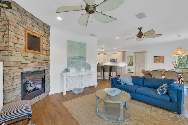 living room featuring a fireplace, light hardwood / wood-style floors, ceiling fan, and crown molding