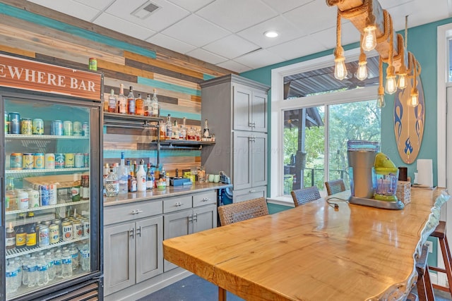 bar with gray cabinetry, a paneled ceiling, wooden walls, and hanging light fixtures