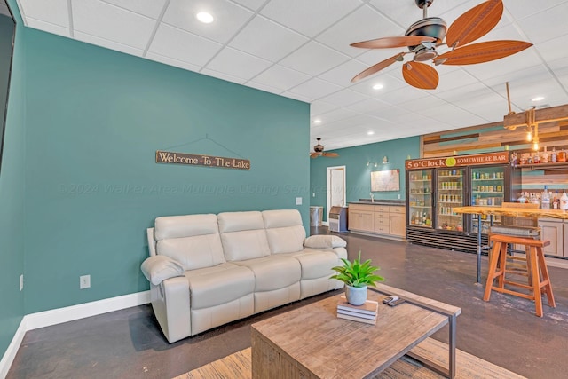 living room featuring a drop ceiling, ceiling fan, indoor bar, and concrete floors