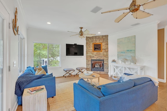 living room with ceiling fan, a stone fireplace, light wood-type flooring, and ornamental molding