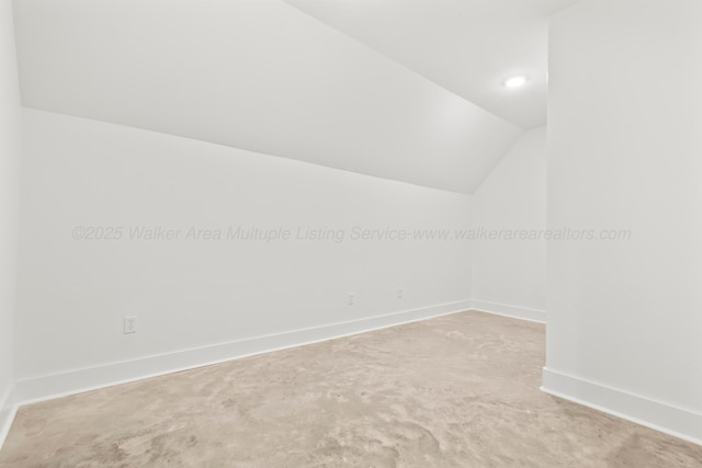 spare room featuring baseboards, lofted ceiling, and concrete flooring