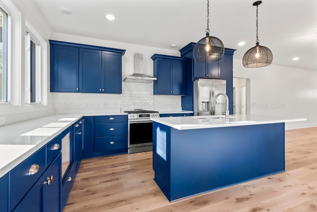 kitchen featuring blue cabinetry, appliances with stainless steel finishes, light wood-type flooring, and wall chimney range hood