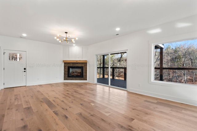 unfurnished living room featuring light wood-type flooring, a notable chandelier, recessed lighting, a fireplace, and baseboards