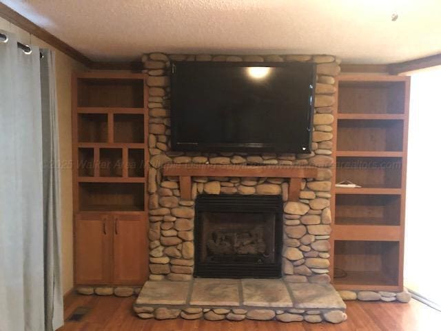 unfurnished living room featuring a textured ceiling, wood finished floors, a fireplace, and ornamental molding