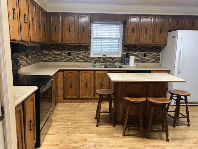 kitchen featuring freestanding refrigerator, a breakfast bar, a sink, black electric range, and light wood-type flooring