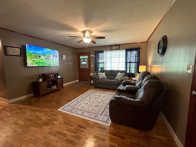 living area featuring baseboards, ceiling fan, wood finished floors, and ornamental molding