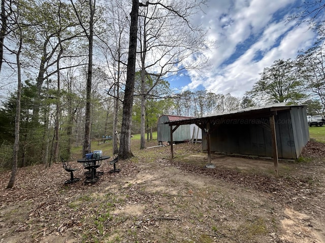 view of yard with a pole building, an outbuilding, a carport, and dirt driveway
