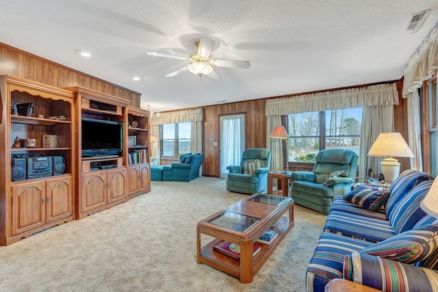 living area featuring carpet floors, ceiling fan, a healthy amount of sunlight, and wooden walls