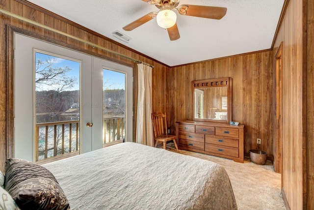 carpeted bedroom featuring access to exterior, visible vents, wooden walls, and ornamental molding