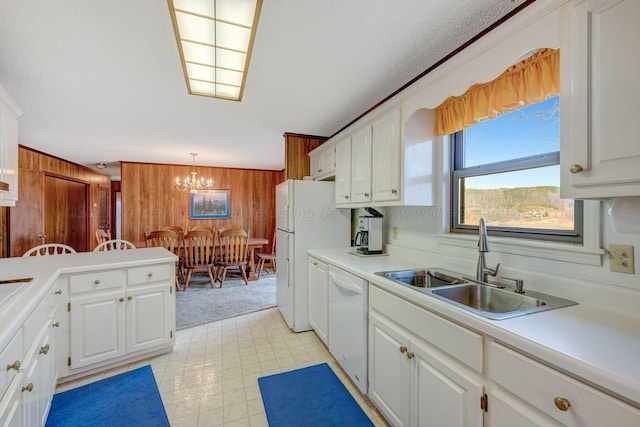 kitchen with white appliances, a notable chandelier, wooden walls, and white cabinetry