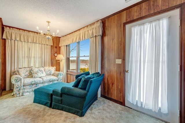 carpeted living area featuring an inviting chandelier, crown molding, wooden walls, and a textured ceiling