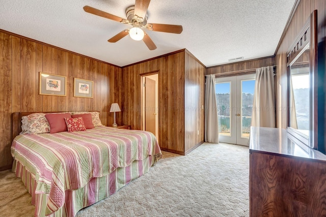 bedroom featuring a textured ceiling, wood walls, access to exterior, french doors, and light colored carpet