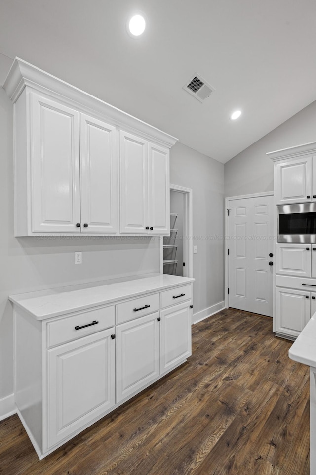 kitchen featuring stainless steel microwave, light countertops, white cabinetry, and vaulted ceiling