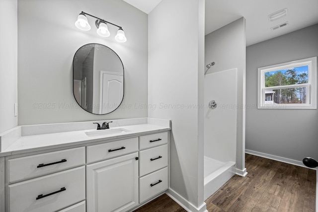 full bathroom with wood finished floors, vanity, a walk in shower, and visible vents