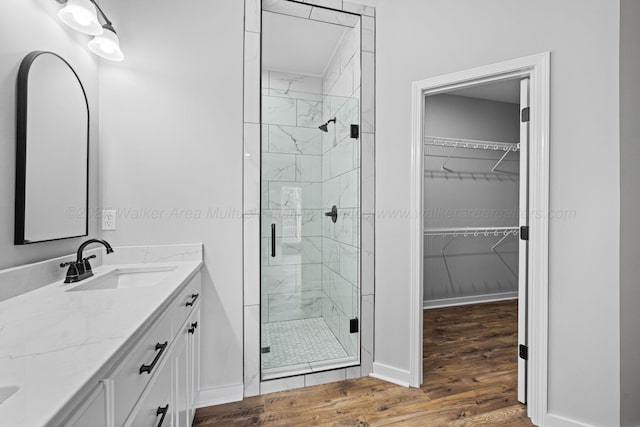 bathroom featuring wood finished floors, vanity, a walk in closet, and a shower stall