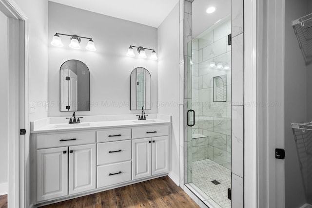 bathroom featuring double vanity, a sink, a stall shower, and wood finished floors