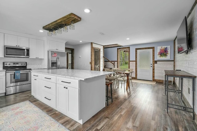 kitchen featuring recessed lighting, white cabinetry, wood finished floors, a kitchen island, and appliances with stainless steel finishes