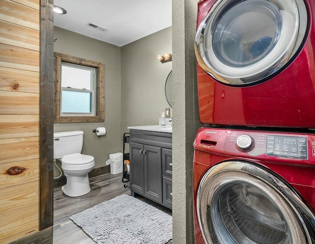 bathroom featuring toilet, visible vents, wood finished floors, stacked washer / drying machine, and vanity