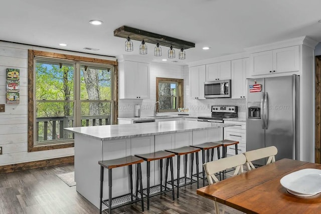 kitchen with dark wood-style floors, a sink, a kitchen island, appliances with stainless steel finishes, and white cabinetry