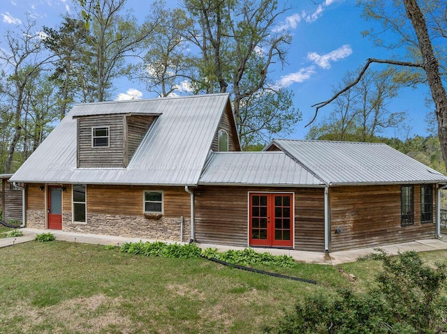 rear view of property featuring stone siding, a lawn, and metal roof
