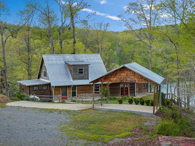 view of front of property with driveway, covered porch, a wooded view, and metal roof