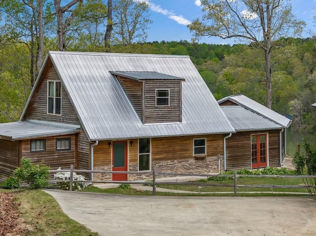 view of front of property with covered porch, a fenced front yard, stone siding, and metal roof