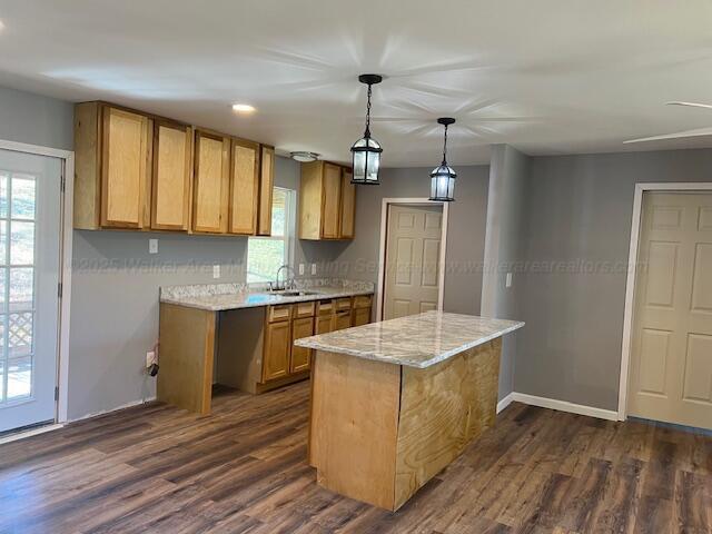 kitchen featuring dark wood-style flooring, baseboards, a sink, decorative light fixtures, and a center island