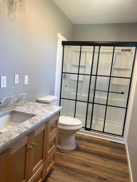 bathroom featuring a stall shower, toilet, wood finished floors, and vanity