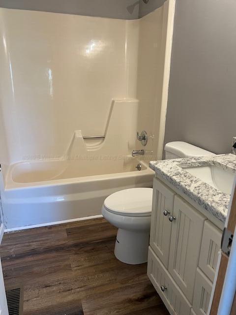 bathroom with visible vents, wood finished floors, toilet, vanity, and shower / washtub combination