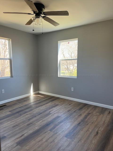spare room with baseboards, dark wood-style flooring, ceiling fan, and a healthy amount of sunlight