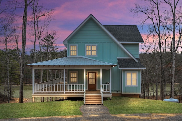 view of front of property with covered porch, a shingled roof, a lawn, and board and batten siding