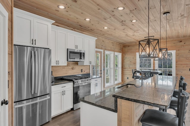 kitchen with a kitchen island with sink, wood walls, wood ceiling, white cabinets, and appliances with stainless steel finishes