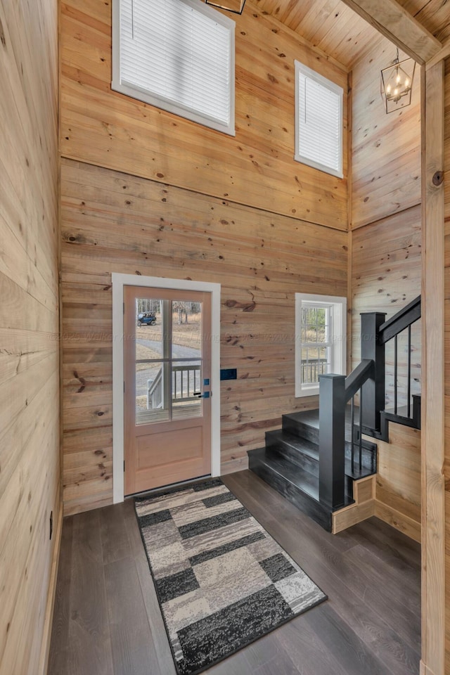 entrance foyer featuring dark wood-style floors, wood walls, stairway, and a towering ceiling