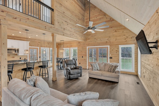 living room featuring a ceiling fan, a towering ceiling, wood finished floors, wood walls, and recessed lighting