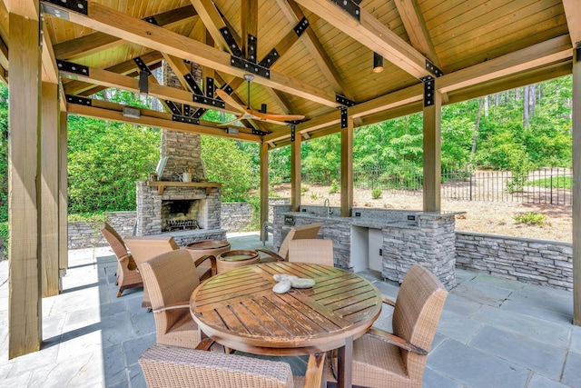 view of patio featuring outdoor dining space, a gazebo, an outdoor stone fireplace, and fence